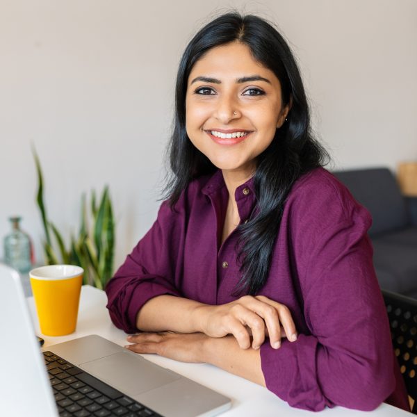 Young indian woman smile at camera working with laptop at home